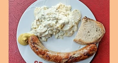 Teller mit Bratwurst, Kartoffelsalat, Senf und Brot in der Huefyse-Bar