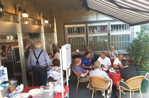 Gäste sitzen an Sommertischen auf der Terrasse vor der Huefyse-Bar