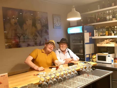 Zwei Stammgäste mit Hüten sitzen am Holztresen der Huefyse-Bar